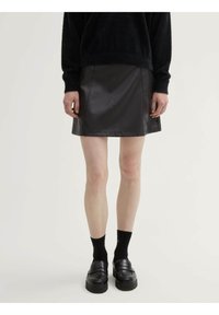 Minifalda de cuero negra con una textura suave, que presenta un corte sencillo y detalles de costura visibles. La lleva puesta con un suéter negro y mocasines.