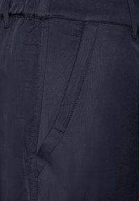 Tessuto blu scuro con una tasca laterale profonda caratterizzata da cuciture dettagliate, parte della fascia elastica visibile nella parte superiore.