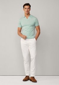 Mentolová, krátkapsová polo košeľa s výstrihom do V. Biele nohavice a hnedé semišové topánky dokončujú outfit. Minimalistický dizajn, bez vzorov.