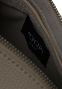 Beige tekstuuri sisepind kotis, kus on must silt valge tekstiga "JOOP! JEANS" hõbedase tõmbluku kõrval.