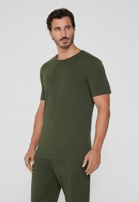 Ciemnozielona koszulka z krótkim rękawem, wykonana z miękkiej tkaniny, z okrągłym dekoltem i dopasowanym krojem. Gładka tekstura bez widocznych wzorów.