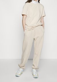 Beige bomull t-shirt och matchande sweatpants, med hög krage-design. Sneakers är flerfärgade med en framträdande sula.