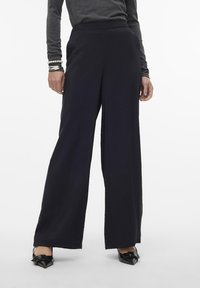 Wijdvallende broek in een donker marineblauwe stof. Beschikt over een hoge tailleband, een soepele textuur en een relaxed fit die tot de enkels valt.