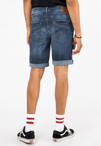 Spijkerbroekshorts met een middelblauwe wassing, opgerolde omslagen en achterzakken. Draag het met zwarte Vans-schoenen en witte sokken met rode strepen.