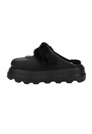 Czarne buty wsuwane z grubą żebrowaną podeszwą i miękką czarną futrzaną wyściółką wokół otworu i górnego paska na stopie.