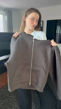 Donkergrijze hoodie met ritssluiting, hoge hals, grote voorzakken en platte naden. Glad stof met een effen kleur en een minimalistisch ontwerp.