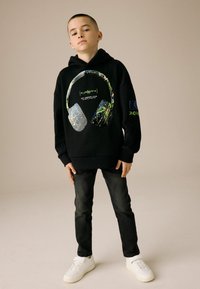 Zwarte hoodie met een grafisch ontwerp van koptelefoons in levendige kleuren. Gecombineerd met donkere jeans en witte sneakers, wat een casual look creëert.