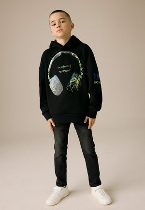 Zwarte hoodie met een grafisch ontwerp van koptelefoons in levendige kleuren. Gecombineerd met donkere jeans en witte sneakers, wat een casual look creëert.