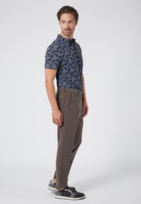 Short-sleeve blue floral shirt paired with brown, textured trousers and black sneakers. Shirt features a button-up collar; pants have pockets.