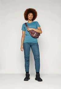 Türkiz rövidujjú póló, hegymintával, világoskék, keskenyített nadrággal párosítva. Barna keresztpántos táska, fekete lábbeli. Egységes textúra és modern dizájn.