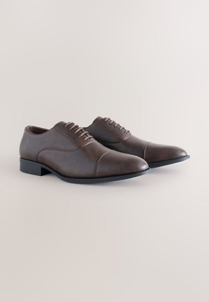 Braune Lederschuhe mit glatter Textur, Schnürdesign, spitzer Zehe und einer kontrastierenden schwarzen Gummisohle. Klassischer und vielseitiger Stil.