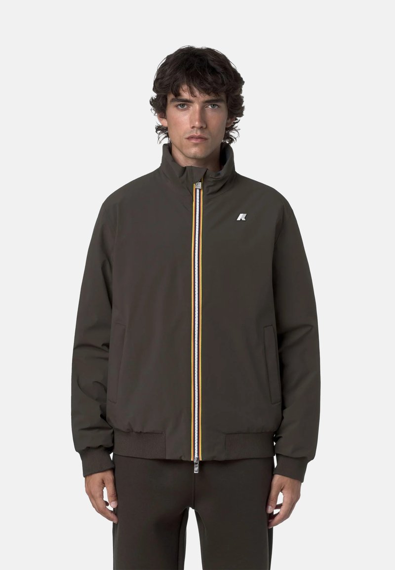 Giacca bomber marrone con polsini a coste, colletto alto e zip frontale con strisce gialle, bianche e rosse. Logo sul petto.