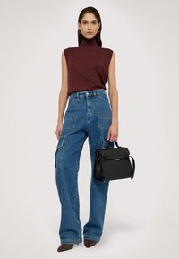Burgundská bezrukávová blůza s vysokým výstřihem, zkombinovaná se světle modrými cargo džíny s bočními kapsami. Černá texturovaná kabelka a špičaté podpatky.