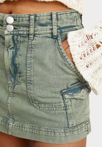 Denimhame vaaleanvihreänä, jossa on haalistunut pinta, kaksi metallinappia, etutaskut ja sivutasku hopeaosilla.