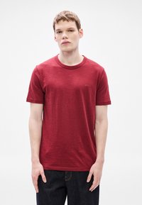 �Κόκκινο κοντομάνικο μπλουζάκι από υφή υφάσματος με στρογγυλή λαιμόκοψη και διακριτικό λογότυπο «BOSS» στο στήθος. Φορεμένο με σκούρο τζιν.