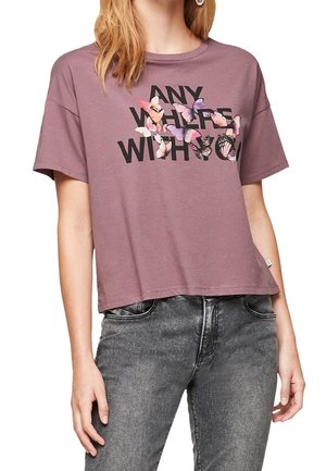 Kobieta nosząca fioletowy krótki t-shirt z czarnym napisem "ANYWHERE WITH YOU", częściowo zakryty wielobarwnymi ilustracjami motyli.