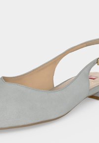 Ανοιχτό γκρι σουέτ γυναικείο παπούτσι μπαλαρίνας με ανοιχτή φτέρνα, μυτερή μύτη και χαμηλό τακούνι σε λευκό φόντο.