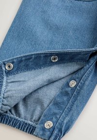 Gros plan sur un tissu denim bleu avec des boutons-pression métalliques le long d’un bord plié et un ourlet cousu.