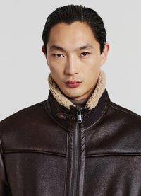 Giacca in pelle marrone con colletto in shearling, chiusura con zip e finitura testurizzata, che presenta dettagli a cucitura orizzontale e un design aderente.