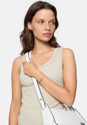 Beige geribbelde tanktop gedragen met een witte schoudertas met zwarte accenten. Een delicaat gouden armbandje is zichtbaar om de pols.