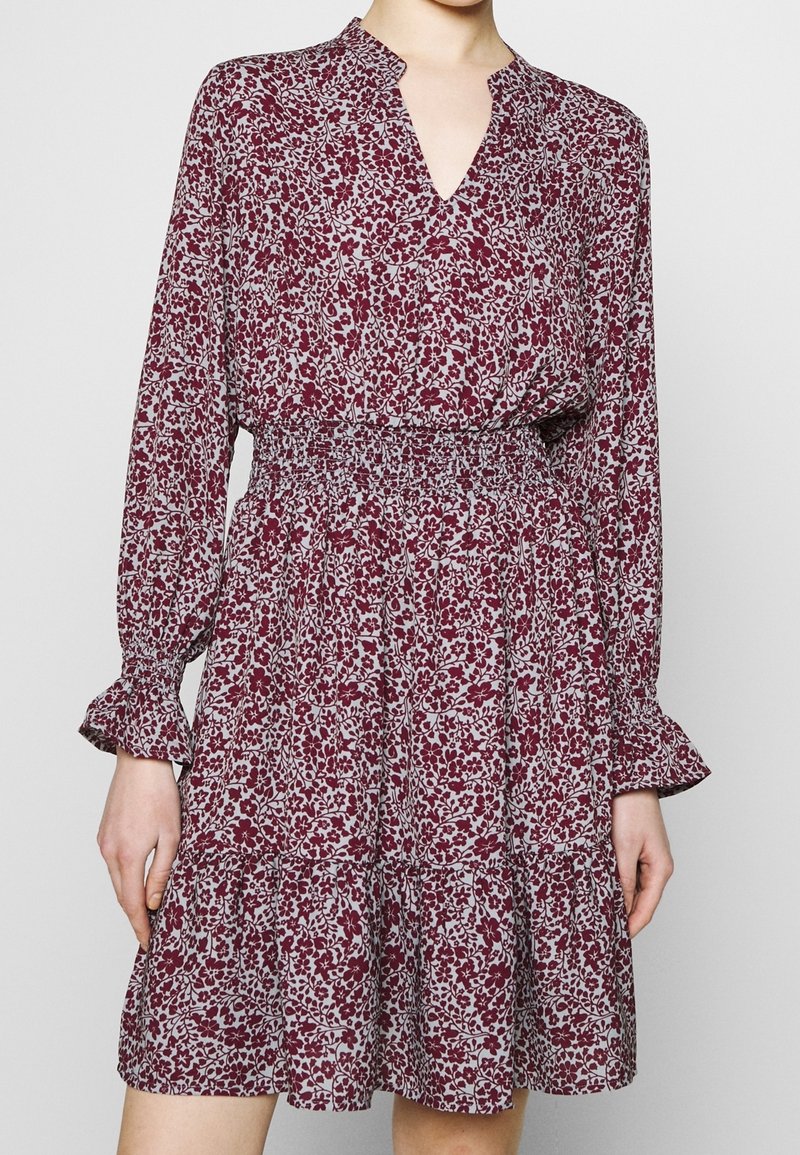 Blommig klänning med ett vinrött och vitt mönster, v-ringning, lång ärm med volanger och smockad midja med en lager-på-lager kjol.