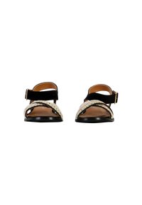 Black suede sandals with woven beige straps, open toe design, adjustable ankle buckle, flat black sole, and smooth inner lining.