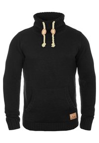 Suéter negro de punto con cuello alto, que incluye cordones crema y un bolsillo frontal. Tejido texturizado con una etiqueta de cuero con marca.