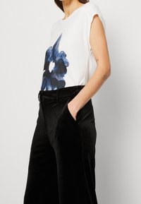 Camiseta blanca con estampado floral azul, de mangas cortas, combinada con pantalones de terciopelo negros de pernera ancha que cuentan con un cinturón y bolsillos laterales.