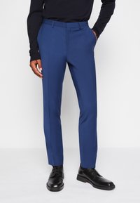 Blaue, maßgeschneiderte Hosen mit schlanker Passform, mit flachem Bund, seitlichen Taschen und subtiler Textur, kombiniert mit schwarzen dress Schuhen.