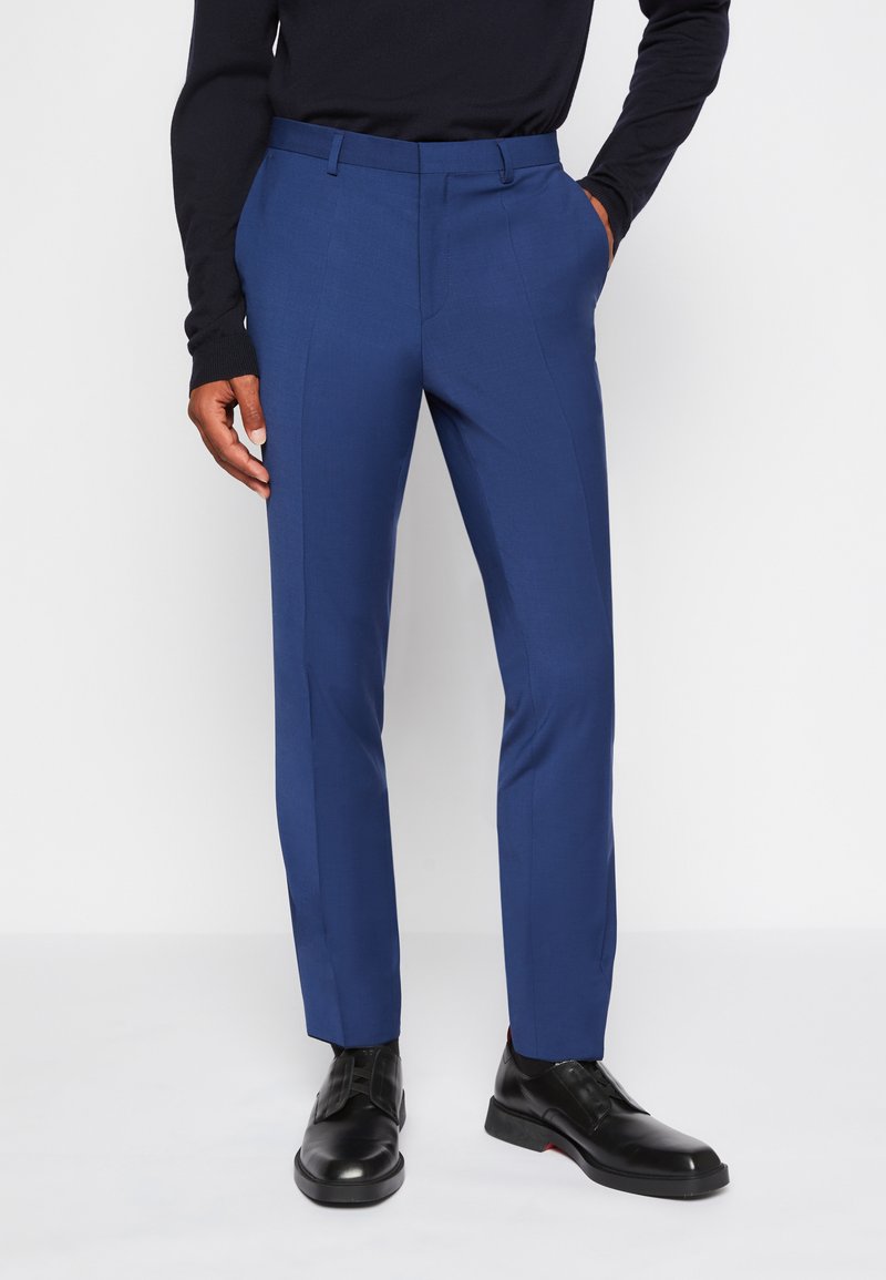 Blaue, maßgeschneiderte Hosen mit schlanker Passform, mit flachem Bund, seitlichen Taschen und subtiler Textur, kombiniert mit schwarzen dress Schuhen.