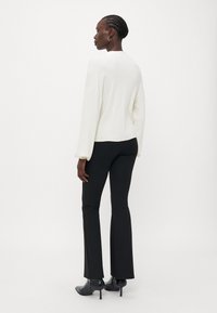Haut à manches longues blanc, coupe décontractée, texture douce, associé à un pantalon évasé noir et des bottines noires. Design simple, détails minimalistes.