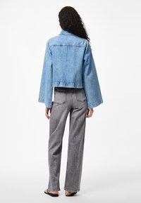 Lyseblå denimjakke med kort modell, vide ermer og klassisk krage. Kombinert med høytlivede grå bukser i strukturert stoff.