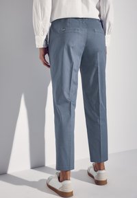 Pantaloni di cotone azzurro chiaro con vestibilità slim, due tasche posteriori e orli cuciti, abbinati a sneaker bianche con suola marrone chiaro.