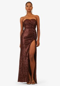Abito da sera senza spalline color bordeaux con paillettes brillanti, spacco alto fino alla coscia e dettaglio della vita attorcigliato. Sandali con tacco completano il look.