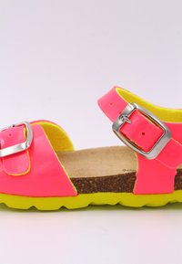 Sandale rose fluo avec une boucle métallique argentée, semelle en liège et semelle extérieure en caoutchouc jaune vif. Cette sandale présente un design à lanières et une surface texturée.