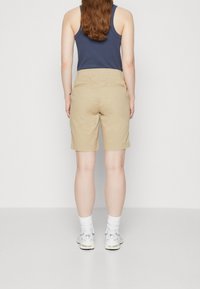 Béžové šortky s hladkou texturou, délka po kolena, se dvěma zadními kapsami. Kombinovány s námořnicky modrým tílkem a bílými sportovními ponožkami a botami.