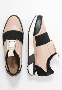 Baskets avec une combinaison de cuir beige, noir et crème, dotées d'une bande élastique texturée noire, d'accents dorés et d'une semelle blanche.