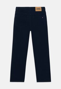 Dark blue straight-leg jeans with a smooth texture, featuring a leather patch on the waistband embossed with "TOMMY HILFIGER" and two back pockets.