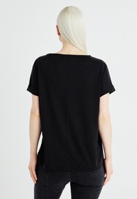 Black short-sleeve t-shirt with a relaxed fit, round neckline, and subtle seam detailing at the back. Smooth, lightweight cotton material.