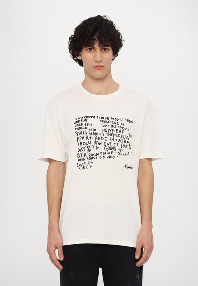 Κρεμ χρώματος oversized μπλουζάκι με μαύρο χειρόγραφο κείμενο στο μπροστινό μέρος, με στρογγυλή λαιμόκοψη και κοντά μανίκια.