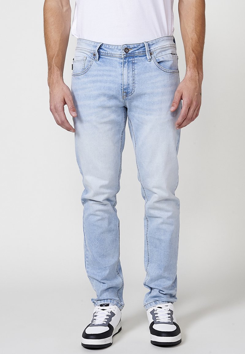 Jeans de mezclilla azul claro con corte recto, cinco bolsillos y un acabado deslavado. Combinados con zapatillas blancas con detalles en negro.