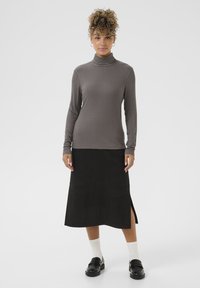 Pelēka ribota garām piedurknēm turtlenecka krekls, savienots ar melnu zamša midi svārku ar sānu šķēlumu, papildināts ar baltām zeķēm un melnajiem mokasīniem.