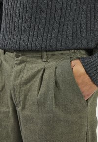 Donkergrijze kabelgebreide trui gecombineerd met saliegroene geplooide broek, met zijzakken en een zachte, gestructureerde stof.