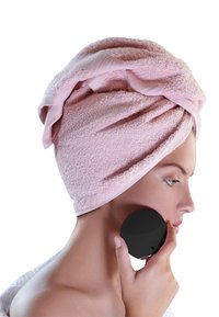 Svart ansiktsrenseapparat holdt mot ansiktet, med teksturert overflate. Subjektet har på seg et rosa håndkle. Huden er glatt og lys.