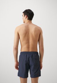 Shorts de înot bărbați în nuanța navy, cu talie elastică și buzunar la spate. Material ușor cu o textură subtilă, tăiați până la înălțimea medie a coapsei.