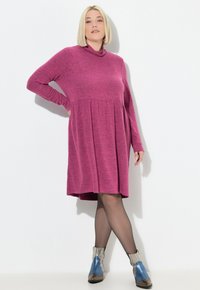 Langarmige coltrui-jurk van roze gemêleerde stof; uitlopende rok met plooien; gecombineerd met metallic blauw- en zilverkleurige enkellaarsjes.