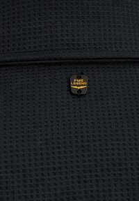 Črna teksturirana tkanina z dvignjenim vzorcem, opremljena z majhno črno označbo, na kateri je v zlatih črkah napisano "PME LEGEND".