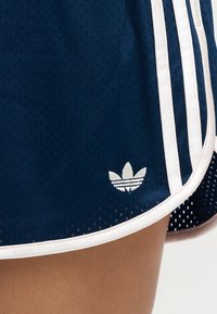 Short de sport bleu marine avec bordure blanche, trois bandes verticales blanches et un logo trefoil Adidas blanc près de l'ourlet.