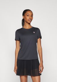 Μαύρη ριχτή κοντομάνικη μπλούζα με στρογγυλή λαιμόκοψη, συνδυασμένη με μαύρη πλισαρισμένη φούστα. Διαθέτει ένα μικρό, πολύχρωμο λογότυπο της μάρκ�ας στην μπλούζα.