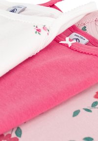 Trzy bawełniane topy na ramiączkach: jeden biały z kwiecistymi akcentami, jeden jednolity różowy oraz jeden jasnoróżowy z kwiecistym wzorem. Wszystkie mają delikatne wykończenia.